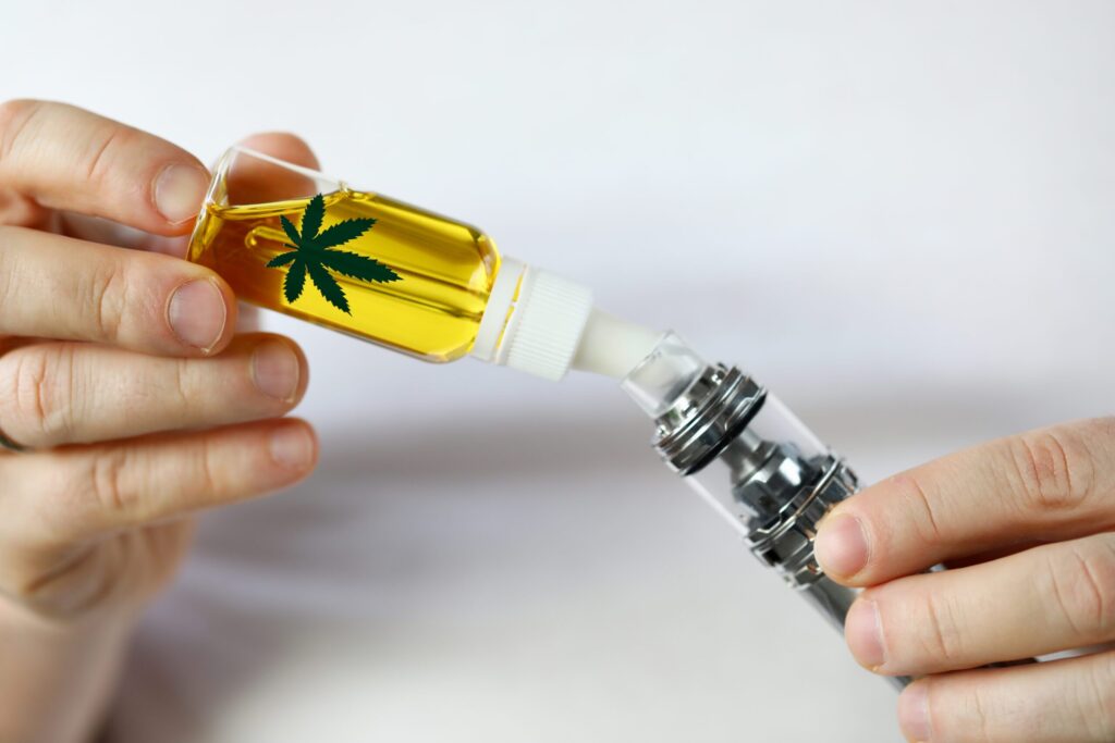 Hands filling a vaping device with a cannabis leaf emblem on the cartridge, illustrating the preparation process for vaping dry herbs.